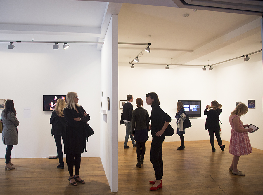 Gallery space with white walls and wooden floors. People are looking at art on the walls.