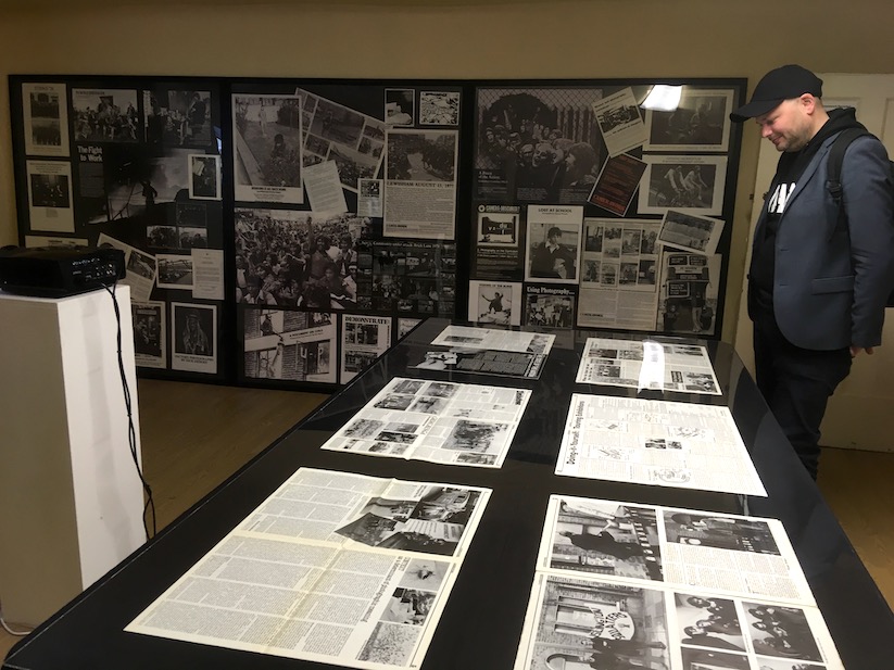 A man looks at spreads of Camerawork magazine arranged on a large black table. 