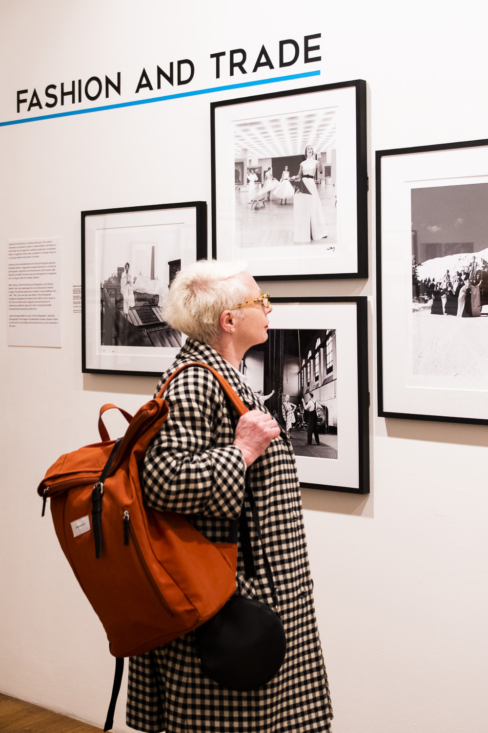 Person with a red bag looks at fashion photographs hung on the gallery wall 